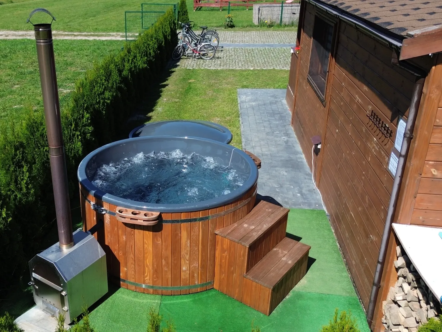 Drewniana balia z jacuzzi przy Domku Na Roztoczu, obok piec opalany drewnem i schodki