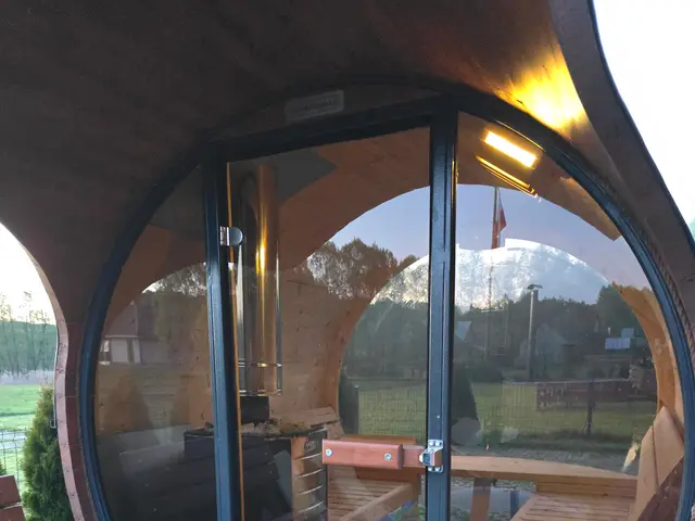 Sauna typu beczka z panoramicznym przeszkleniem, na drewnianym tarasie