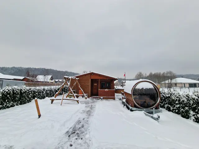 Sauna typu beczka i huśtawka na ośnieżonej działce zimą