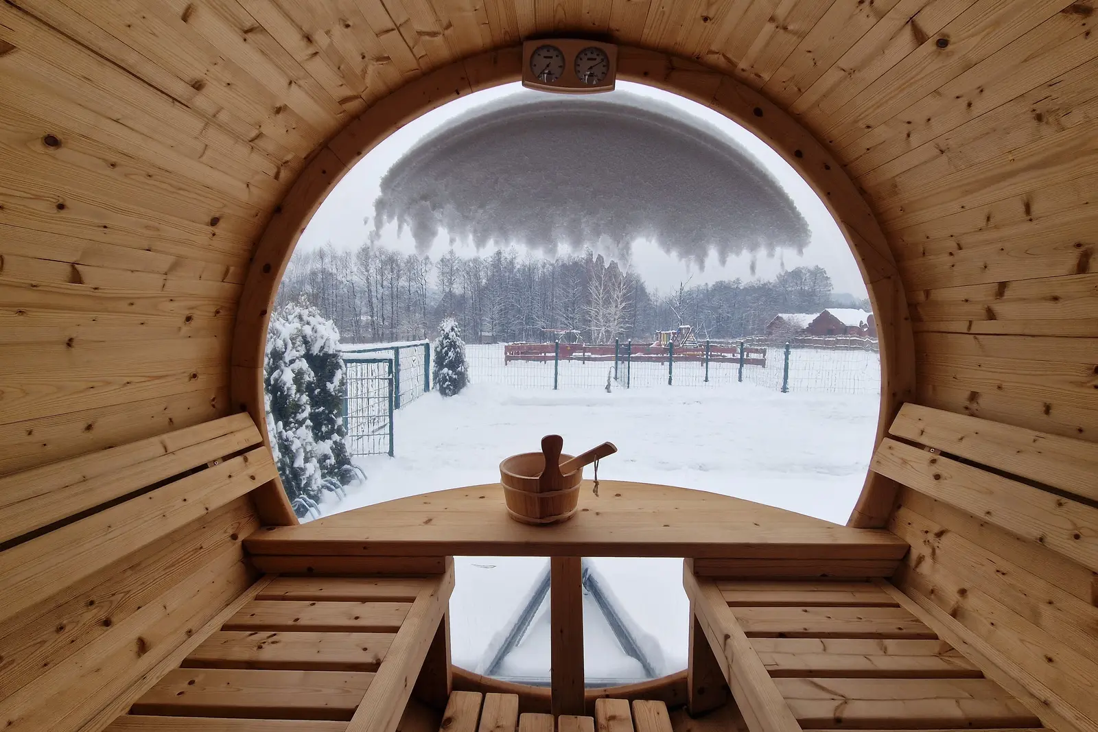 Wnętrze sauny typu beczka z panoramicznym oknem na ośnieżoną działkę Domku Na Roztoczu